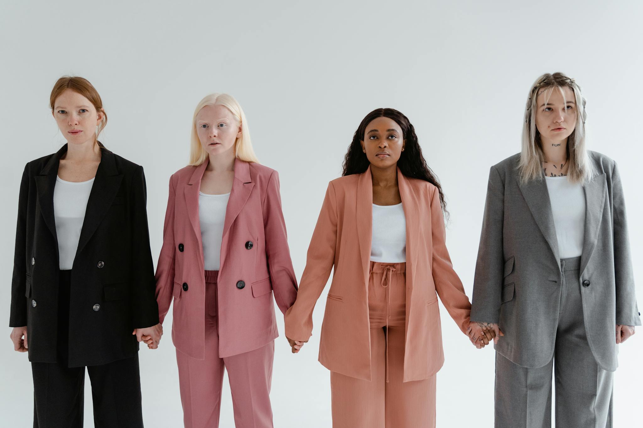 Four diverse women in business suits holding hands against a white background, symbolizing unity.