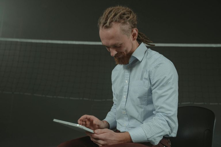 A man sitting with a tablet in an indoor sports hall looking focused.