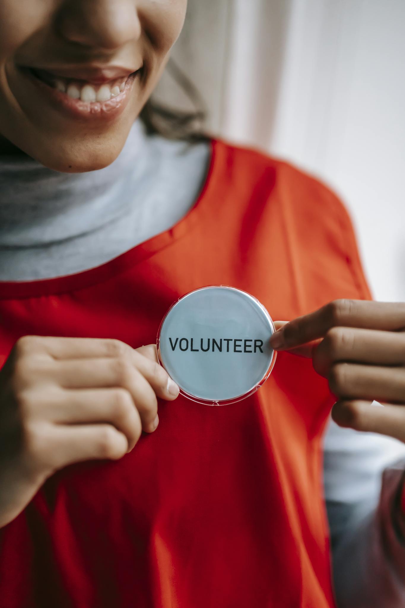 Close-up of a smiling volunteer holding a badge in a bright setting.